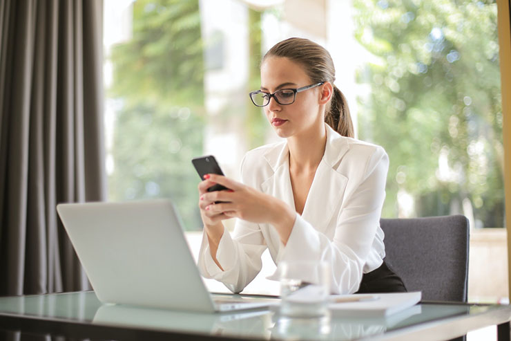 Woman Looking At Phone With Laptop