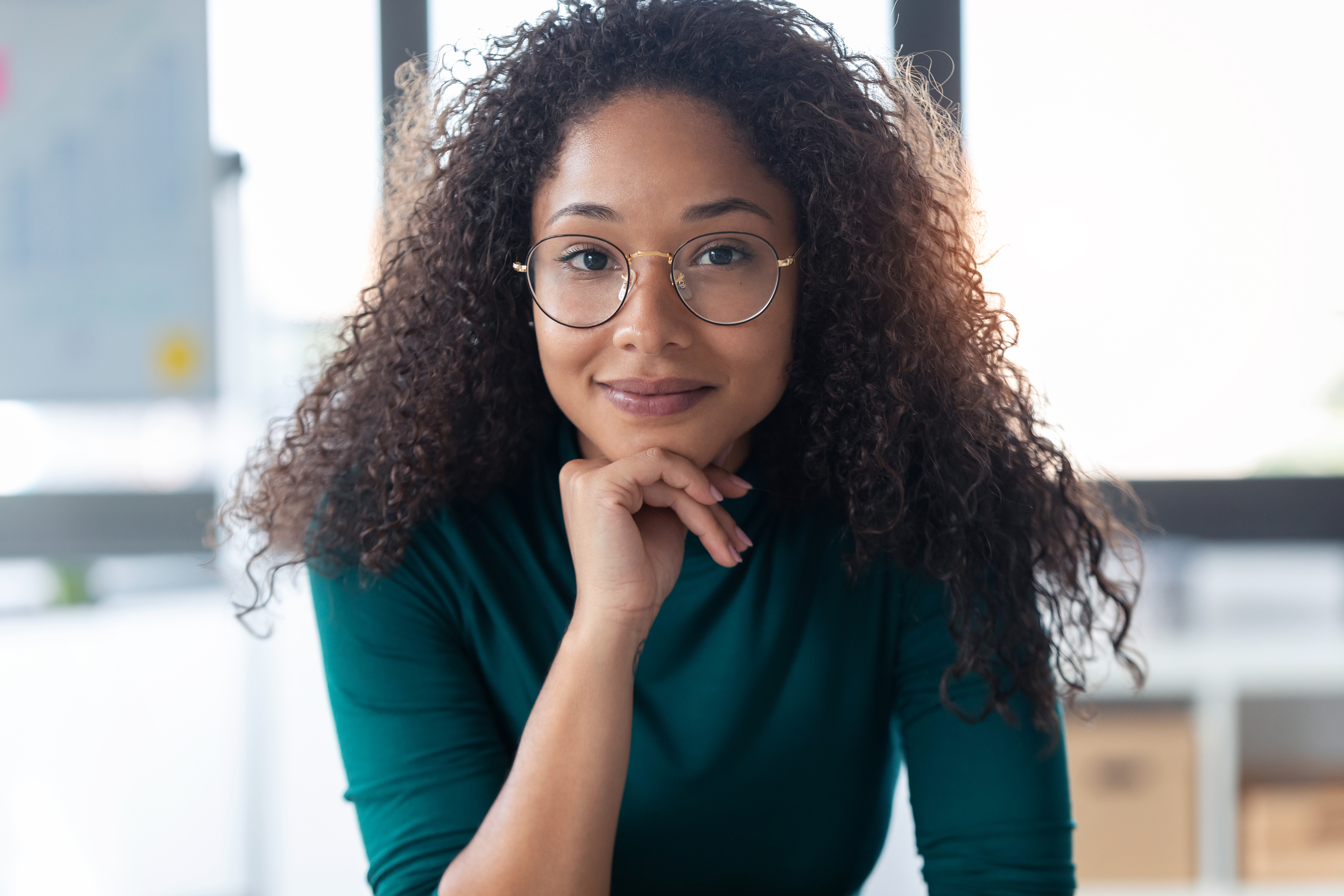 Young black woman in green top with glasses smiling at the camera 